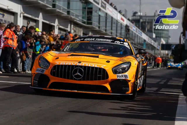 Orange-schwarzer Mercedes-AMG GT3 mit Ravenol-Sponsoring fährt durch die Boxengasse am Nürburgring, im Hintergrund Zuschauer.
