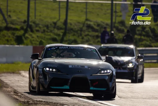 Zwei Rennfahrzeuge auf der Strecke beim Zeittraining, vorne ein Toyota mit grau-schwarzer Lackierung und Gran Turismo Schriftzug.