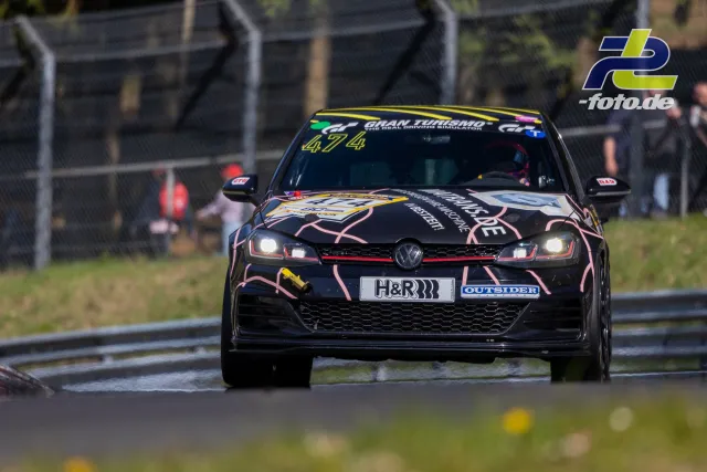 VW Golf GTI TCR #474 mit rosa-schwarzer Lackierung auf der Nordschleife während des Rennens, Frontansicht mit eingeschalteten Scheinwerfern.