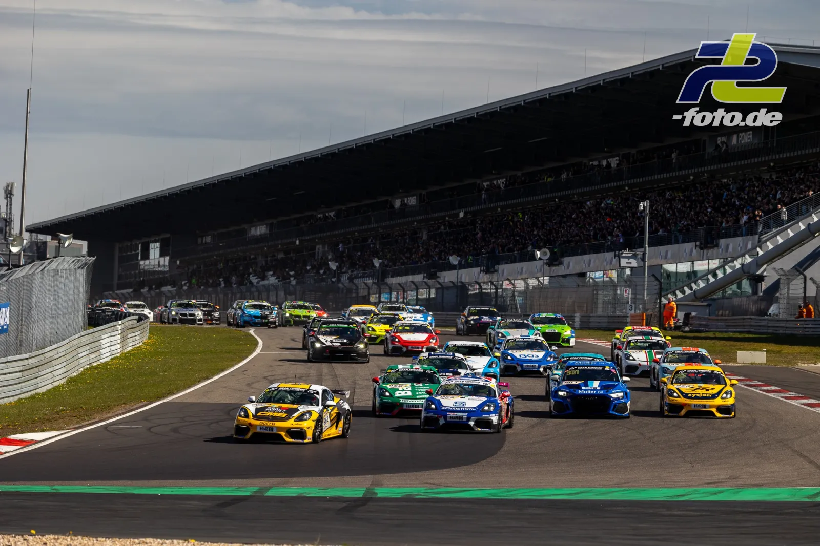 Startfeld in der ersten Kurve nach dem Rennstart auf dem Nürburgring mit GT- und Tourenwagen vor vollbesetzter Tribüne.