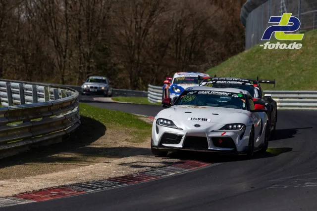 Ein weißer Toyota Supra führt ein Feld durch die Kurve auf der Nordschleife des Nürburgrings.