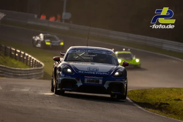 Porsche 718 Cayman GT4 mit blau-weißer Schmersal-Lackierung beim NLS-Zeittraining auf der Nordschleife, verfolgt von weiteren GT-Fahrzeugen.