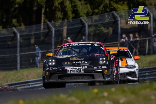 Zwei Porsche 911 GT3 Cup im Zweikampf auf der Nordschleife, führender schwarzer Wagen mit rotem Dach vor weißem mit orangen Spiegeln.