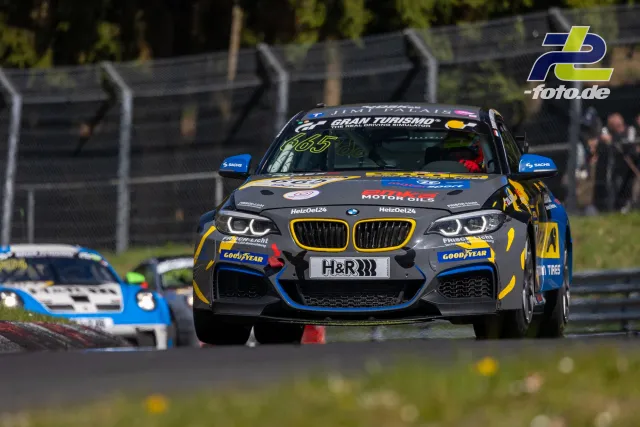 BMW M240i #665 in dunkelgrau-gelb-blauer Lackierung im NLS-Rennen auf dem Nürburgring, verfolgt von weiteren Fahrzeugen.
