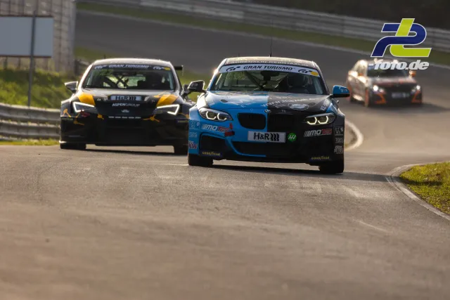Zwei Rennwagen kämpfen in einer Kurve auf dem Nürburgring, vorn ein BMW in blau-schwarz, dahinter ein Fahrzeug in gelb-schwarz.