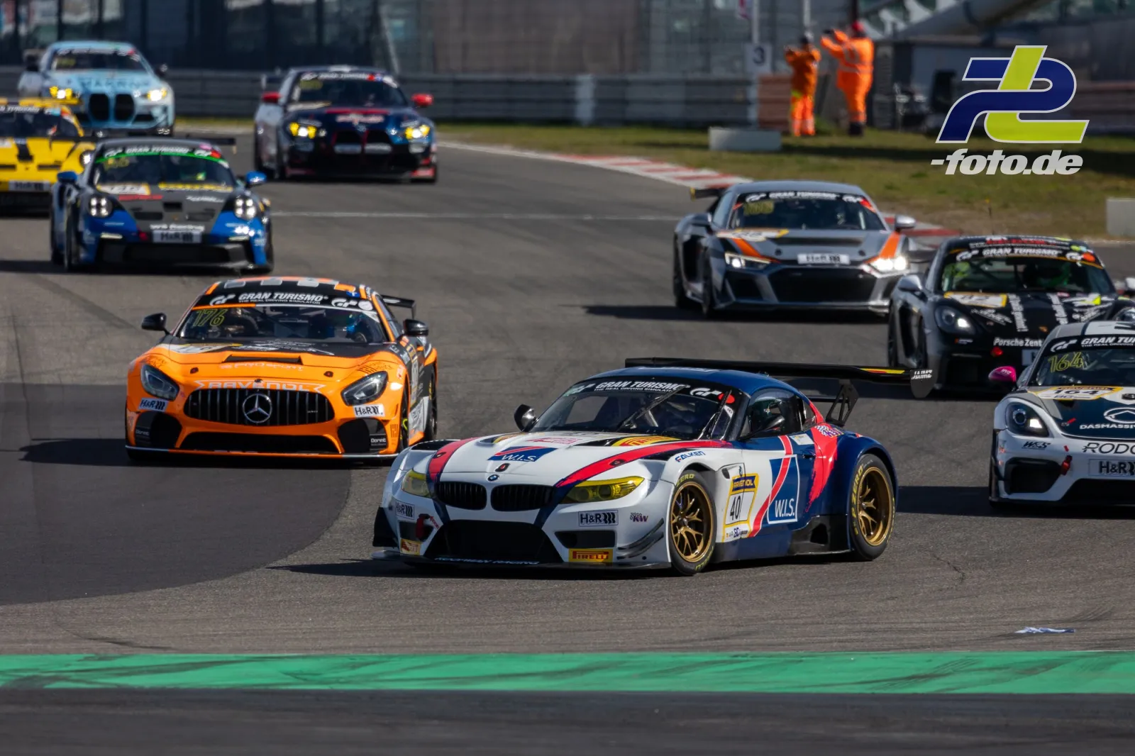 Mehrere GT-Fahrzeuge in einer Kurve auf dem Nürburgring, angeführt von einem BMW Z4 GT3 in Weiß-Rot-Blau und einem orangefarbenen Mercedes-AMG GT.