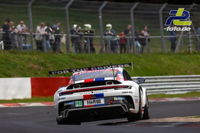 Porsche 911 GT3 R von Black Falcon in Kurve auf dem Nürburgring, Heckansicht mit Zuschauern hinter Fangzaun.