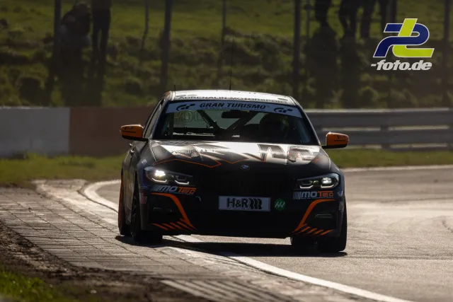 Rennwagen mit schwarz-oranger Lackierung auf der Nordschleife beim Zeittraining, Randstein im Vordergrund