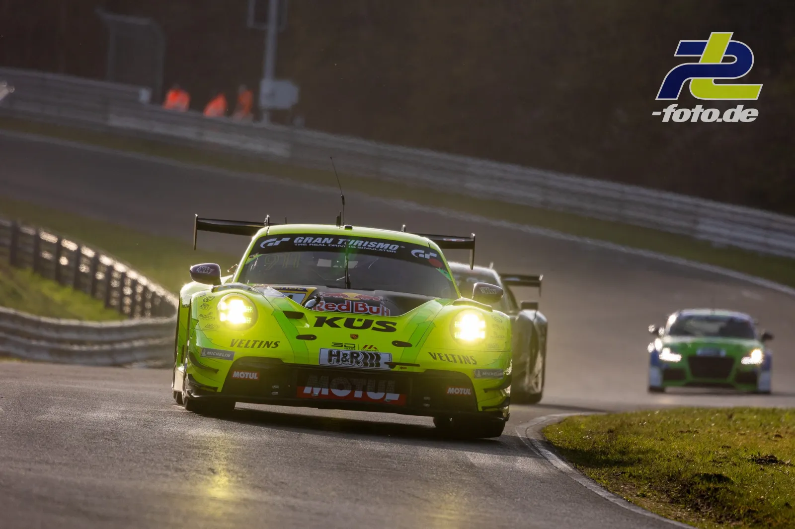 Neongelber Porsche 911 GT3 R mit Red Bull-Sponsoring in der Kurve auf dem Nürburgring, gefolgt von einem weiteren Fahrzeug.