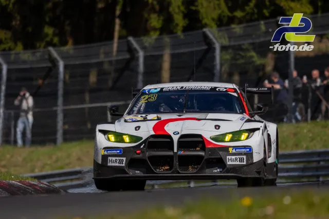 BMW M4 GT3 mit Startnummer 23 in weißer Lackierung mit roten Akzenten auf der Nordschleife bei Tageslicht.