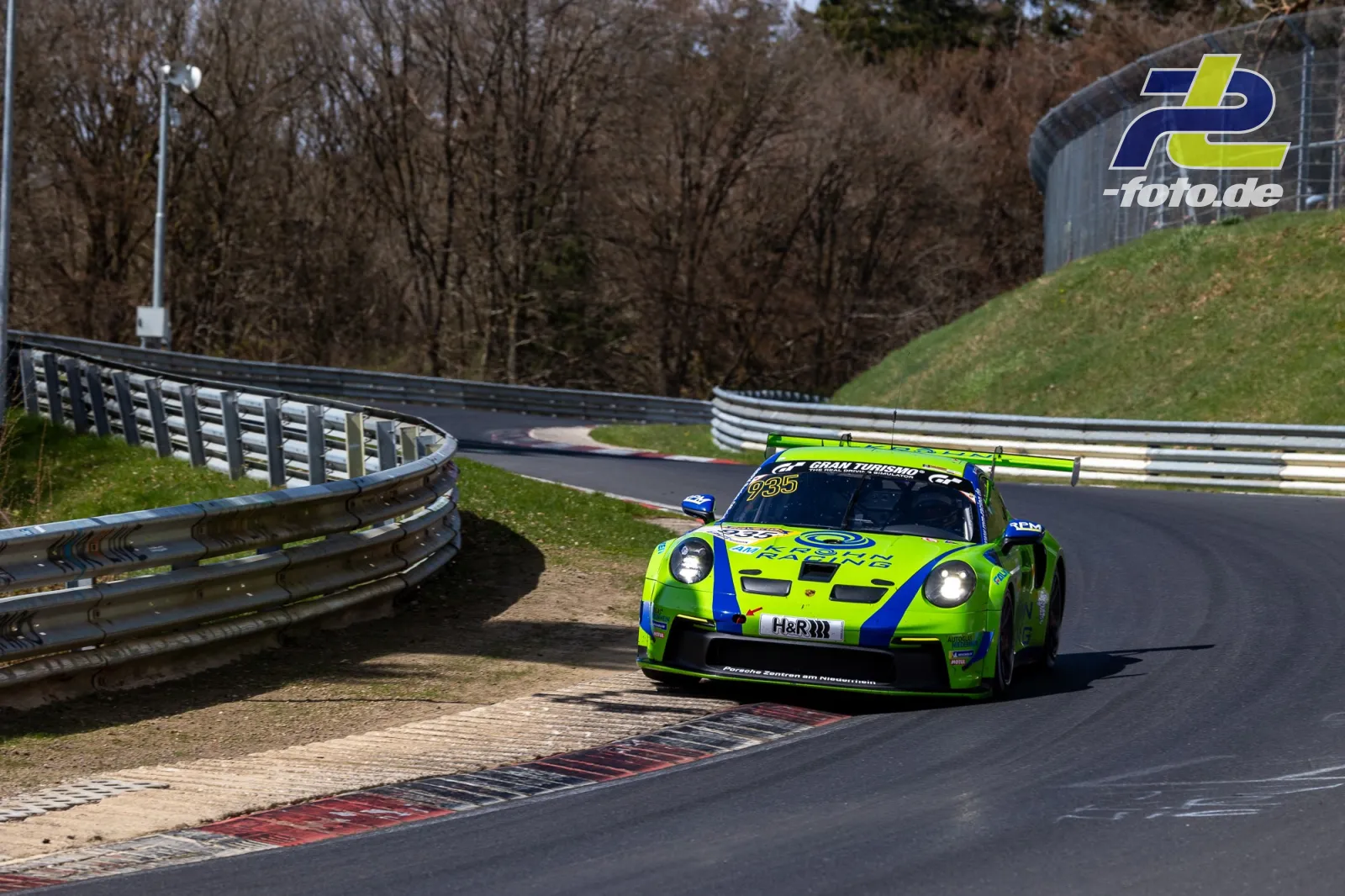 Porsche 911 GT3 R in auffälliger neongelb-blauer Lackierung auf der Nordschleife des Nürburgrings in einer Kurve.