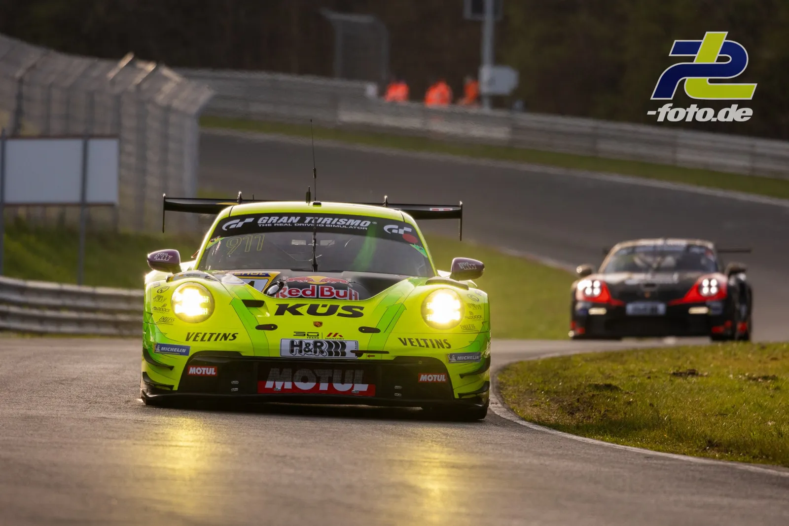Porsche 911 GT3 R in neongelb-grüner Lackierung führt auf der Nordschleife vor einem schwarzen GT-Sportwagen während des Trainings.