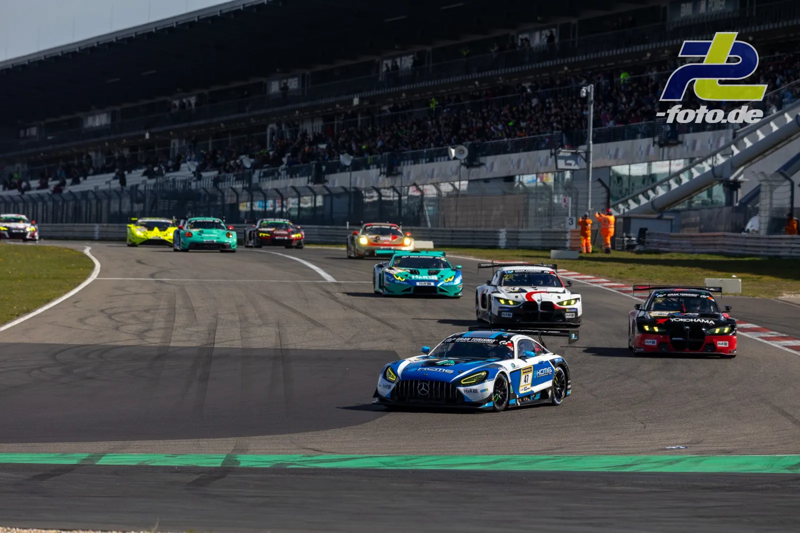 GT3-Fahrzeuge in Rennformation auf der Nordschleife, Tribüne mit Zuschauern im Hintergrund