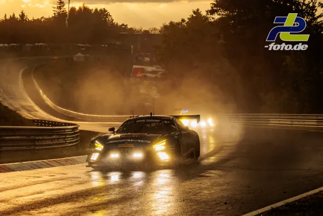 GT3-Rennwagen im Gegenlicht auf nasser Strecke am Nürburgring, weitere Fahrzeuge folgen durch Gischt.