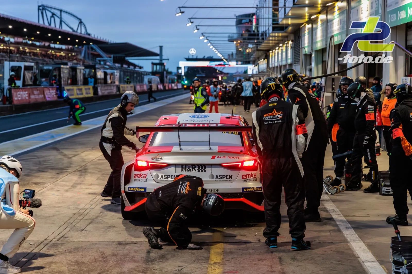 Audi RS3 LMS SEQ bei Boxenstopp in der Dämmerung während des 24h-Rennens am Nürburgring, Mechaniker beim Reifenwechsel.