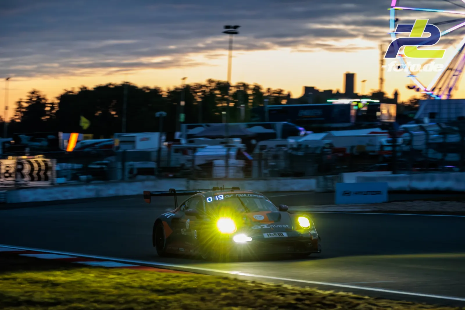 Porsche 911 GT3 R mit Startnummer 4 in der Abenddämmerung mit eingeschalteten Scheinwerfern auf der Rennstrecke.