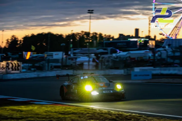Porsche 911 GT3 R mit Startnummer 4 in der Abenddämmerung mit eingeschalteten Scheinwerfern auf der Rennstrecke.