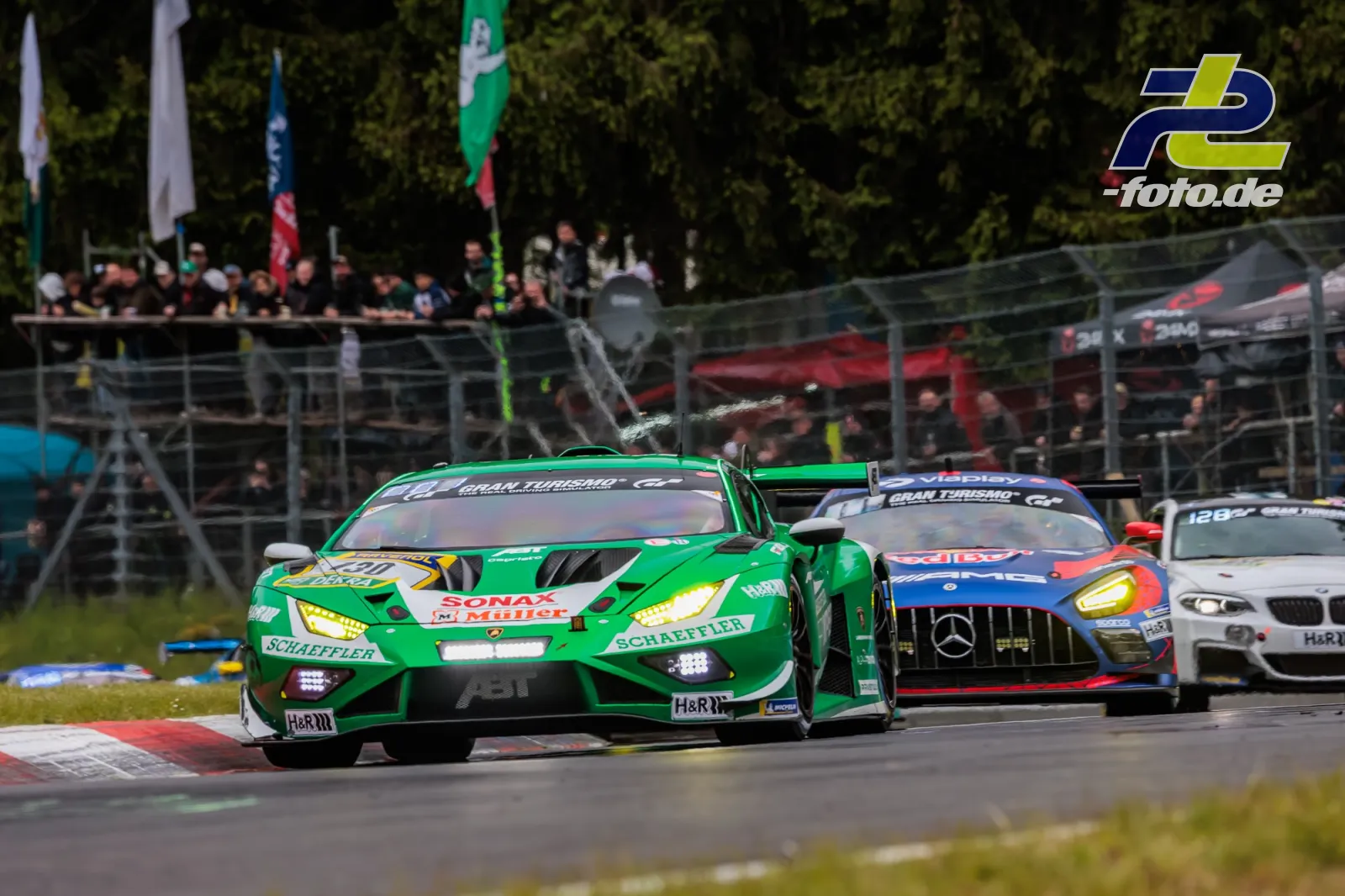 Drei GT3-Fahrzeuge im Rennen auf der Nordschleife, grüner Lamborghini führt vor Mercedes-AMG und BMW, Zuschauer an der Strecke.