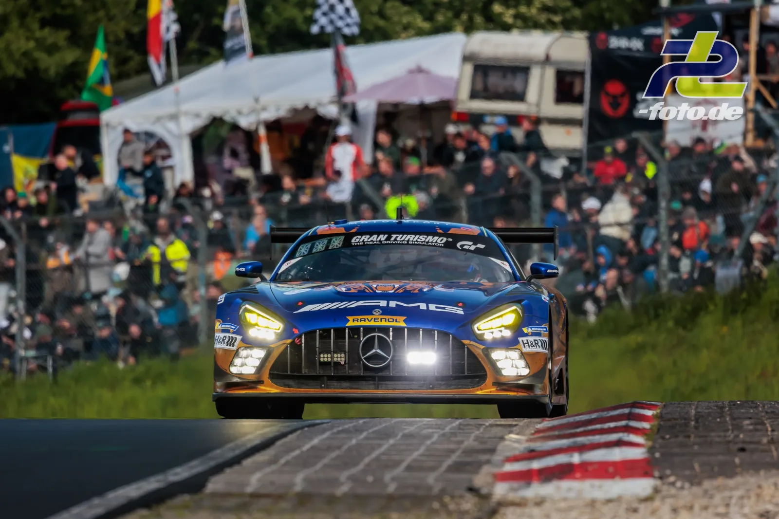 Mercedes-AMG GT3 in blau-oranger Lackierung fährt auf dem Nürburgring vor voller Tribüne während des 24h-Rennens.