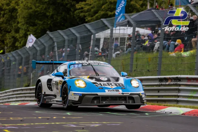 Porsche 911 GT3 R Nummer 123 in Blau-Weiß auf der Nordschleife beim 24h-Rennen, Zuschauer im Hintergrund.
