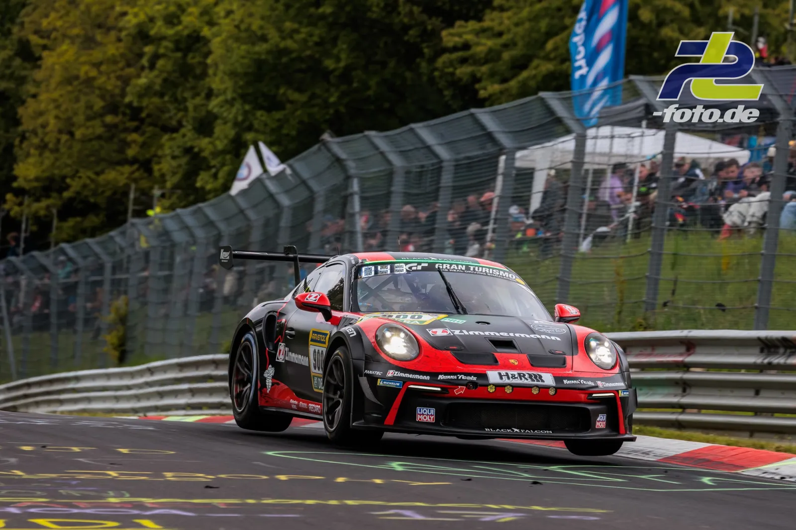 Porsche 911 GT3 Cup in Rot-Schwarz während des 24h-Rennens auf der Nürburgring-Nordschleife, Tribüne im Hintergrund.