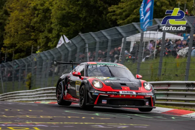Porsche 911 GT3 R Nummer 900 in schwarz-roter Lackierung auf der Nordschleife beim 24h-Rennen, Tribüne im Hintergrund.