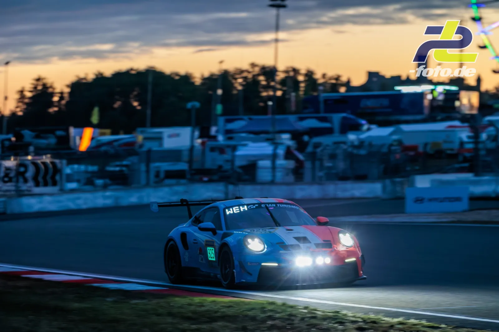 Porsche 911 GT3 R #925 bei Dämmerung mit eingeschalteten Scheinwerfern auf dem Nürburgring während des 24-Stunden-Rennens.