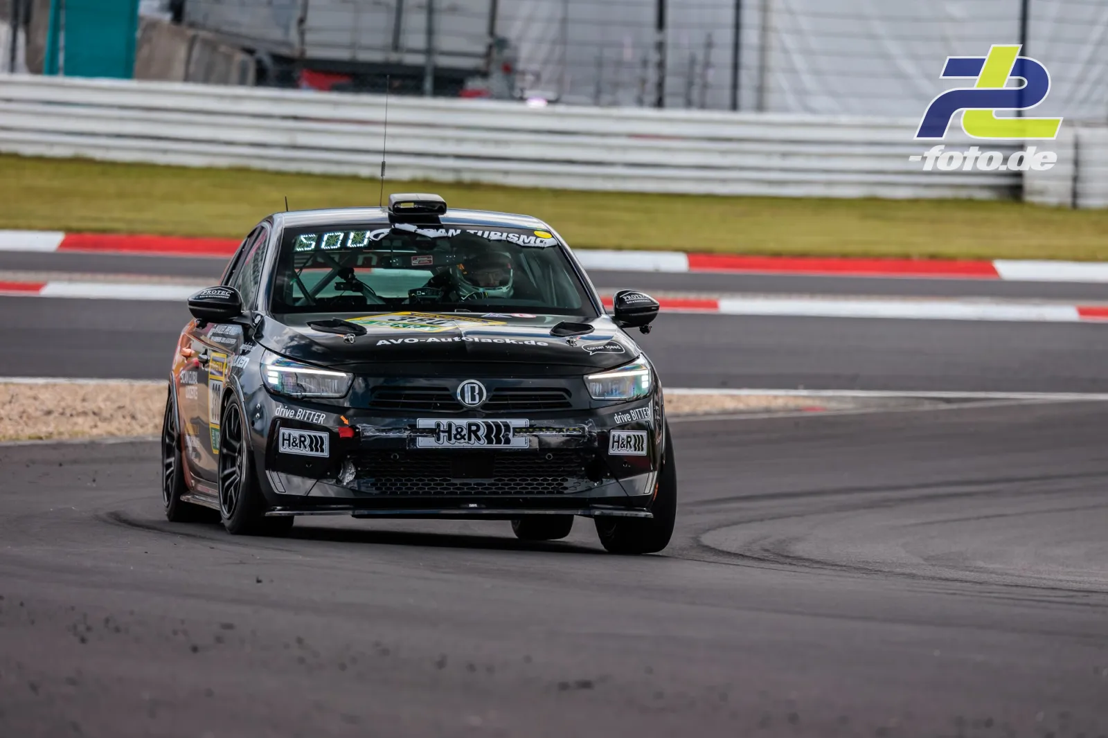 Schwarzer Tourenwagen mit H&R-Sponsoring während des Qualifyings auf dem Nürburgring. Fahrzeug in Kurve mit rot-weißem Randstein im Hintergrund.