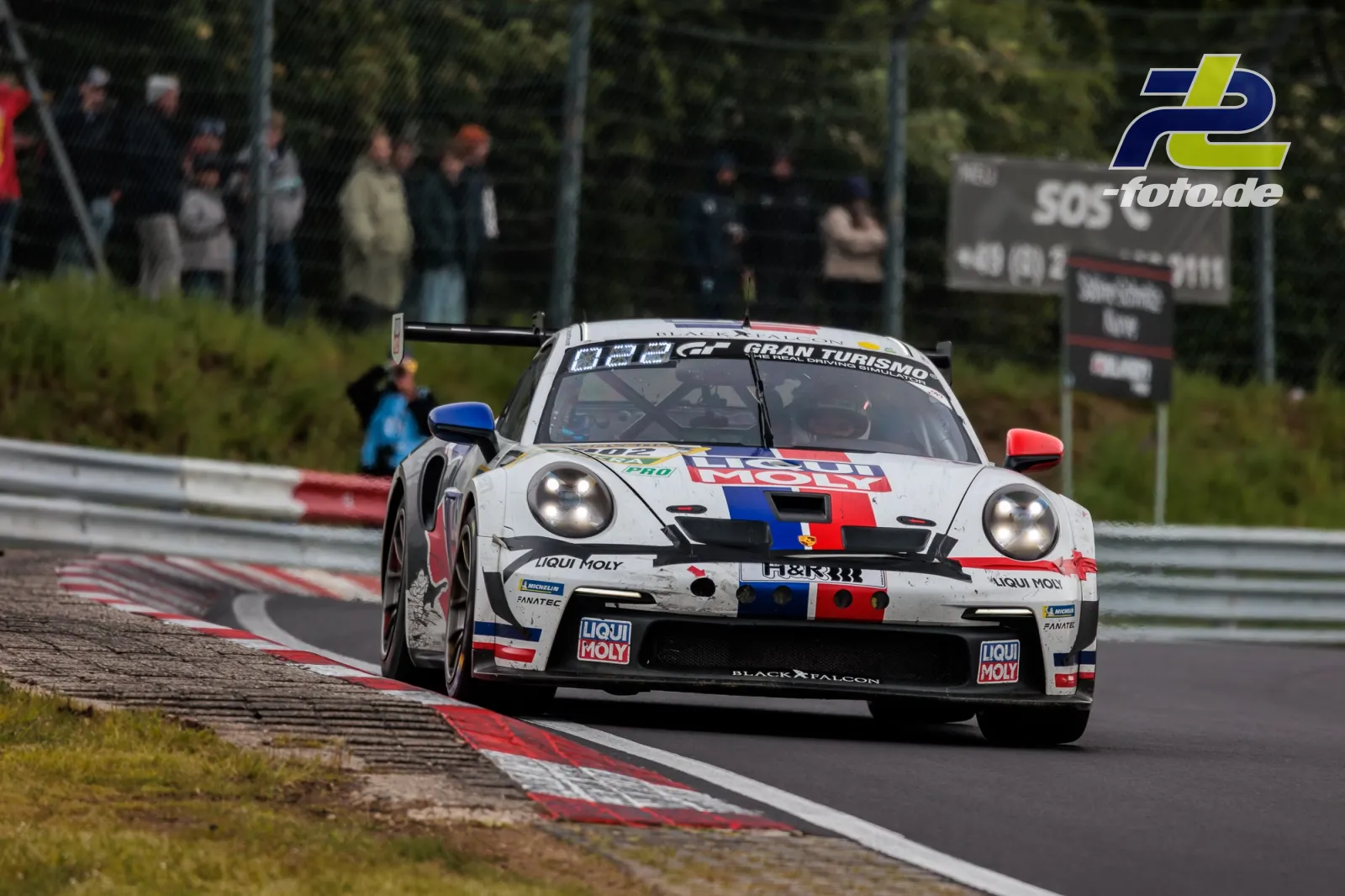Porsche 911 GT3 Cup in weiß-rot-blauer Lackierung auf der Nürburgring Nordschleife beim 24h-Rennen mit Zuschauern im Hintergrund