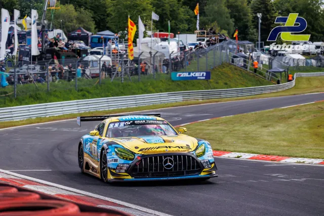 Mercedes-AMG GT3 Nr. 26 in gelb-blauer Lackierung in einer Kurve auf dem Nürburgring, Zuschauer im Hintergrund.