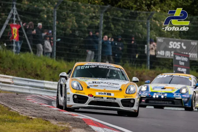 Zwei Porsche Cayman im Rennen auf der Nordschleife des Nürburgrings, Zuschauer an der Strecke.