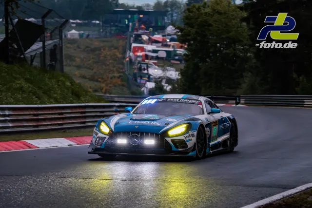Mercedes-AMG GT3 mit Licht auf nasser Strecke in Kurve auf der Nordschleife, Fahrerlager im Hintergrund, Nürburgring Qualifying.