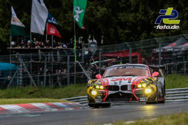 BMW Z4 GT3 in Kurve auf dem Nürburgring beim 24-Stunden-Rennen, Zuschauertribüne und Fahnen im Hintergrund