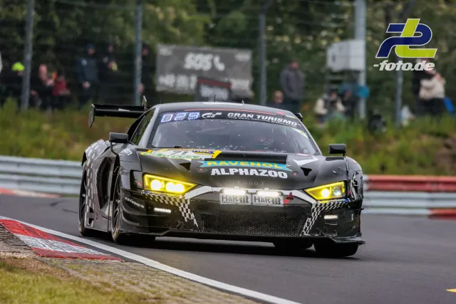 Audi R8 LMS GT3 mit gelben Scheinwerfern auf der Nordschleife während des 24h-Rennens, Zuschauer im Hintergrund.