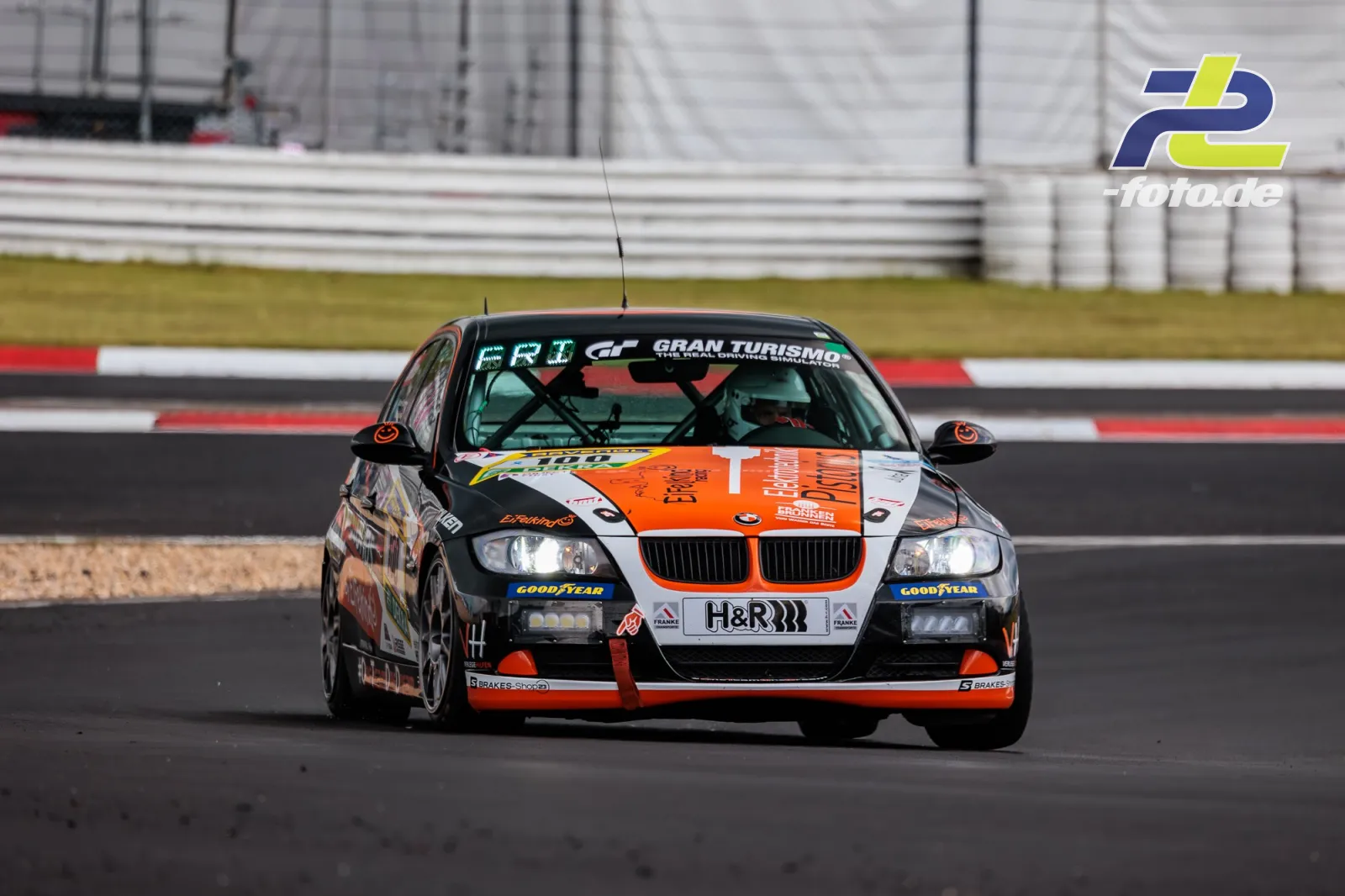 BMW 325i #100 in Kurve während Qualifying zum ADAC RAVENOL 24h Nürburgring 2026, orange-schwarz-weiße Lackierung.