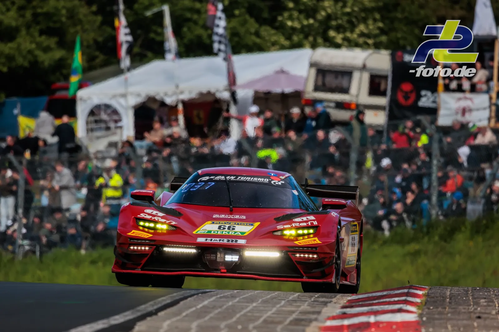 Roter Rennwagen mit Startnummer 66 auf der Nordschleife vor Zuschauerkulisse beim 24h-Rennen am Nürburgring.