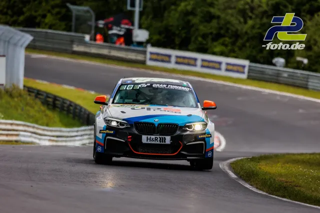 BMW mit weiß-blau-orangefarbener Lackierung in Kurve auf der Nürburgring-Nordschleife beim 24h-Rennen Qualifying.
