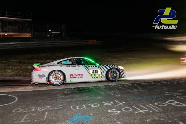 Porsche 911 Cup mit Startnummer 415 nachts auf der Nordschleife, Langzeitbelichtung zeigt Lichtspuren vorbeifahrender Fahrzeuge.