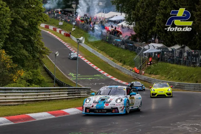 Formationsrunde beim 24h-Rennen Nürburgring: Porsche 911 GT3 führt das Feld durch eine Kurve, Zuschauer mit Rauchfackeln im Hintergrund