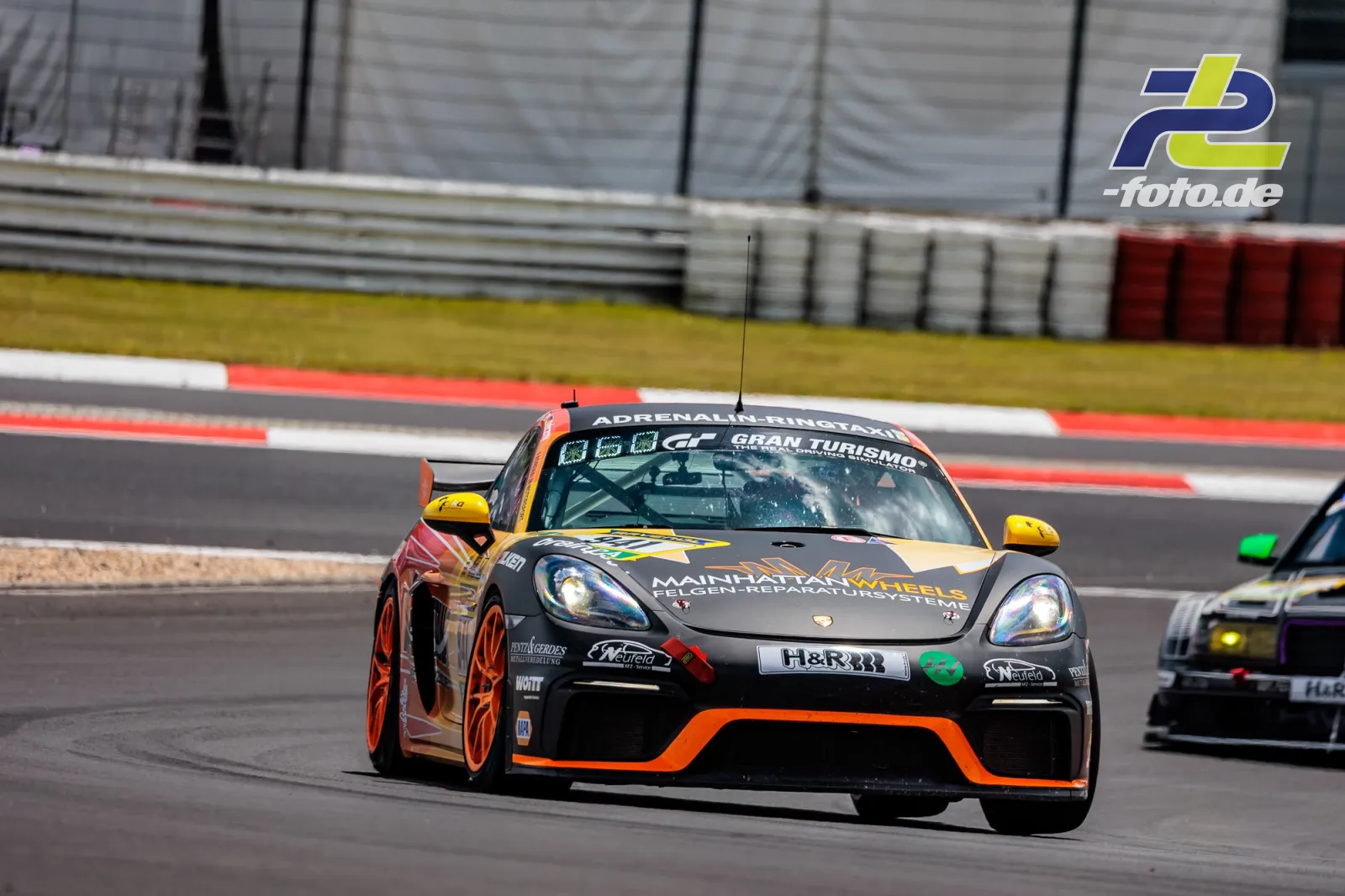 Porsche Cayman GT4 in schwarz-oranger Lackierung im Qualifying auf dem Nürburgring, zweites Fahrzeug folgt im Hintergrund.