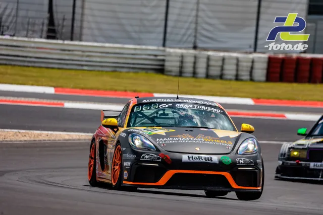 Porsche Cayman GT4 in schwarz-oranger Lackierung im Qualifying auf dem Nürburgring, zweites Fahrzeug folgt im Hintergrund.