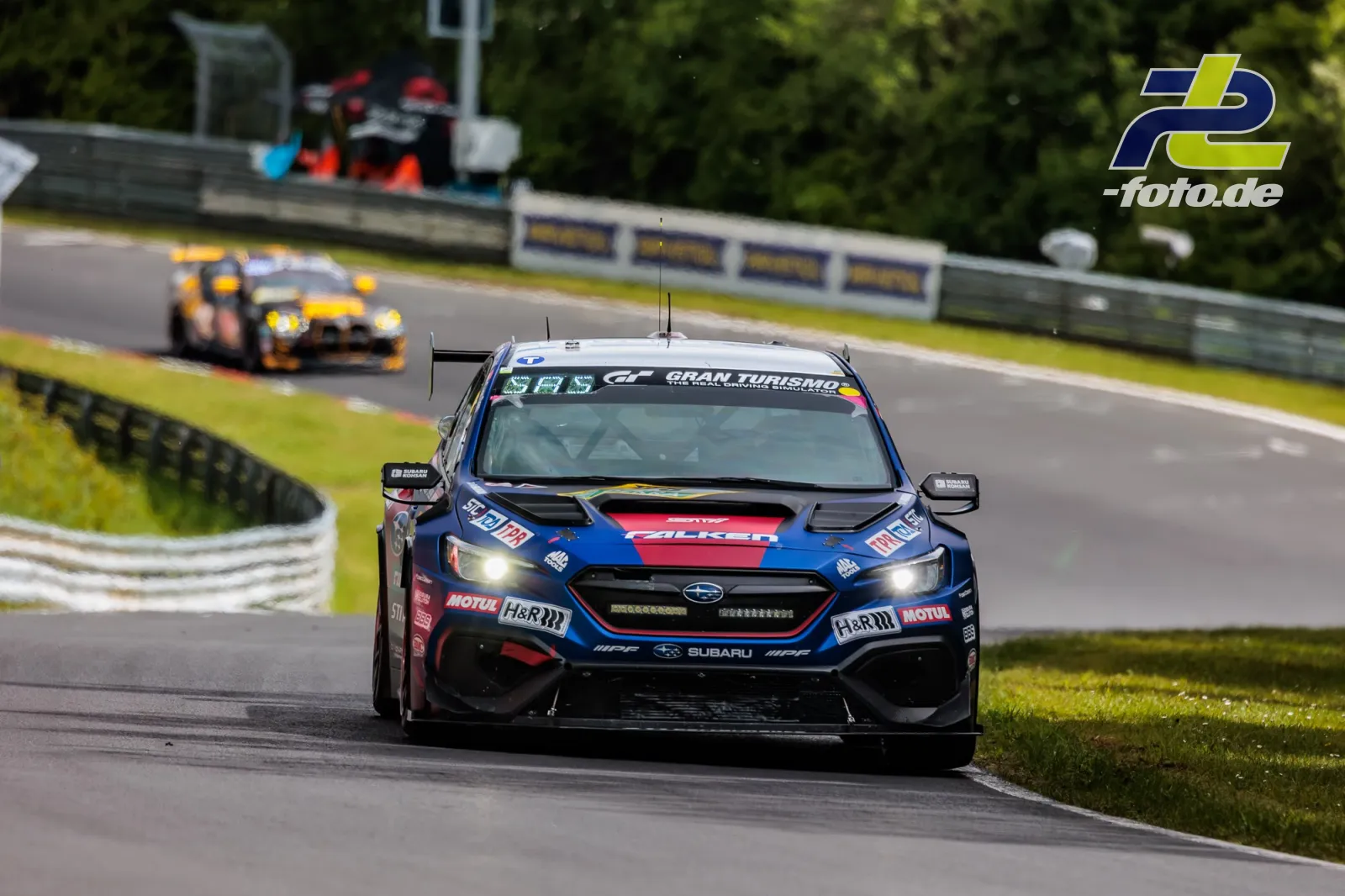 Subaru-Rennwagen in blau-roter Lackierung auf der Nordschleife, gefolgt von einem gelb-schwarzen Fahrzeug während des Qualifyings zum 24h-Rennen.
