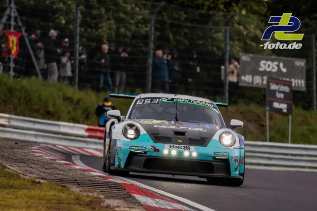 Porsche 911 GT3 R in türkis-weißer Lackierung auf der Nordschleife während des 24h-Rennens mit Zuschauern an der Strecke