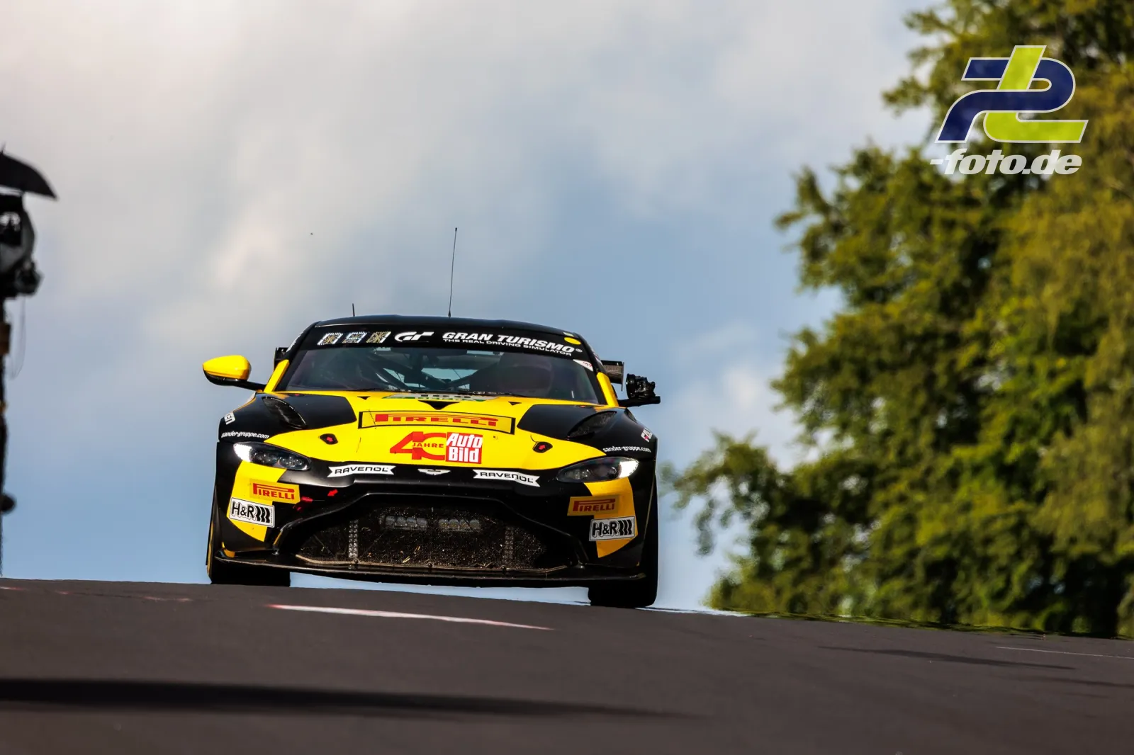 Aston Martin GT4 in gelb-schwarzer Lackierung während des 24h-Rennens über die Bergkuppe springend.