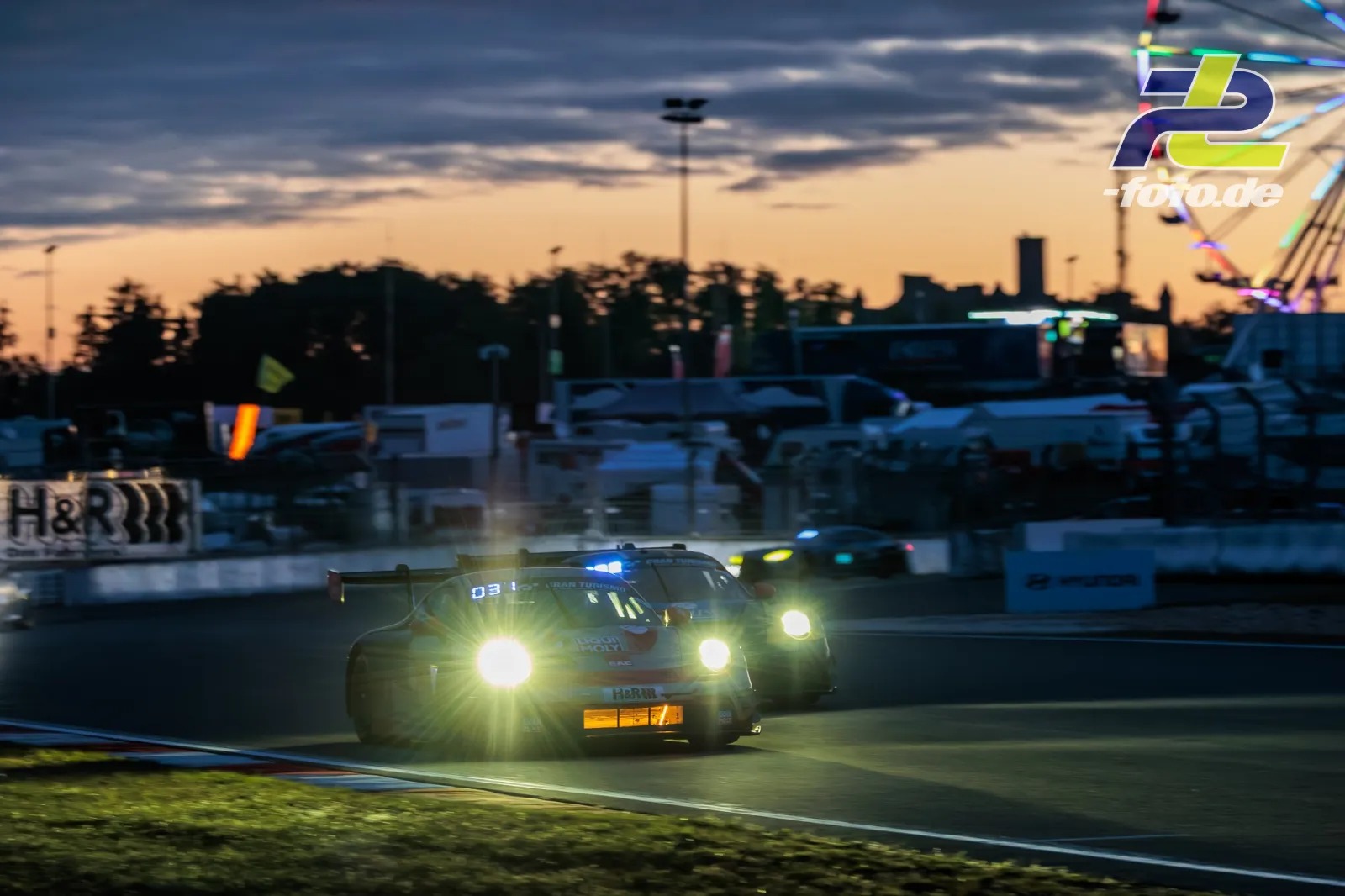 Porsche 911 mit Startnummer 5 in der Abenddämmerung auf dem Nürburgring beim 24-Stunden-Rennen mit eingeschalteten Scheinwerfern.