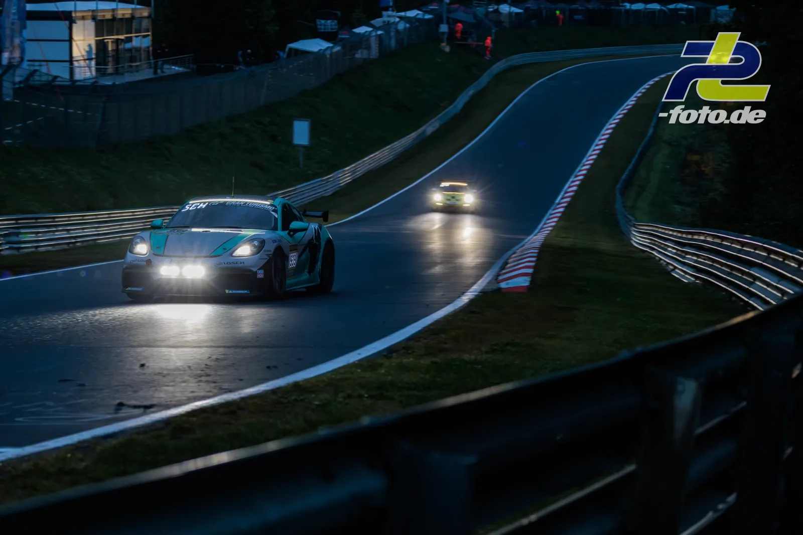 Porsche mit weißer und türkiser Lackierung bei Nachtfahrt auf dem Nürburgring, gefolgt von einem weiteren Fahrzeug.