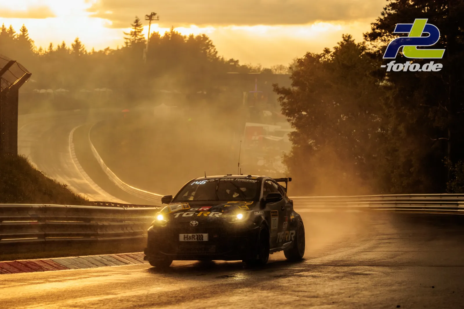 Toyota GR Yaris im Gegenlicht bei Sonnenuntergang auf der Nordschleife des Nürburgrings, atmosphärischer Dunst über der Strecke.