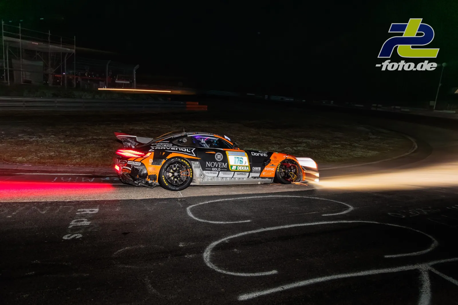 Porsche GT3-Rennwagen bei Nacht auf regennasser Strecke mit leuchtenden Bremsscheiben und Lichtspuren im Hintergrund.