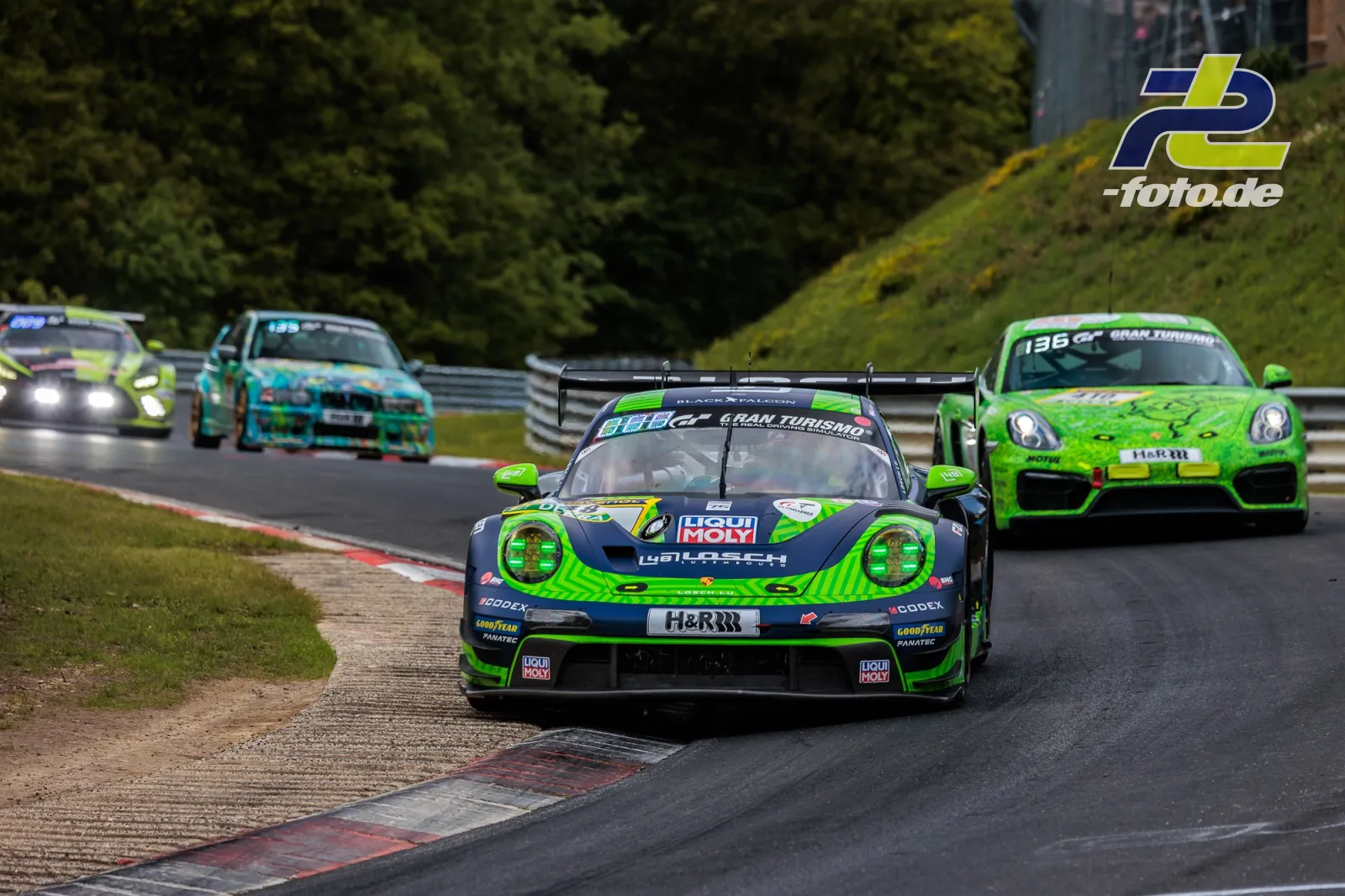 Porsche 911 GT3 R in grün-schwarz führt Fahrzeugfeld durch Kurve beim 24h-Rennen Nürburgring, Wald im Hintergrund.