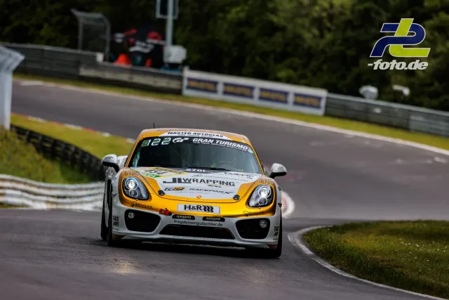 Porsche Cayman GT4 in weiß-gelber Lackierung in Kurve auf der Nürburgring-Nordschleife während des Qualifyings.